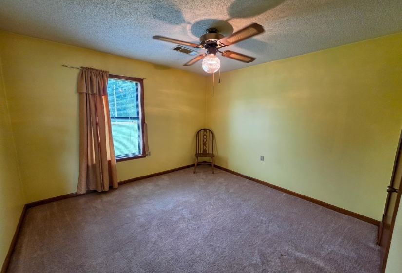 Room with textured carpet flooring, a window featuring wood trim, and a ceiling fan with integrated lighting