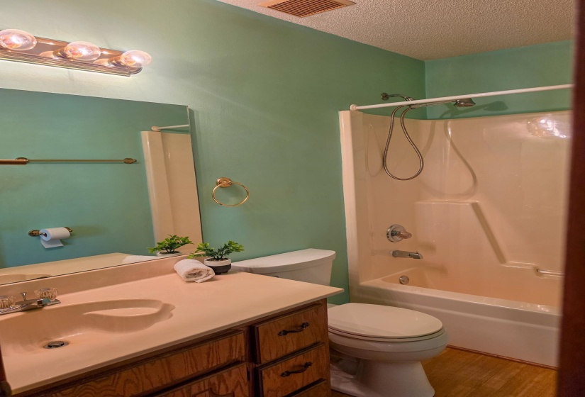 Bathroom featuring a single vanity with an integrated sink and wood-finish cabinetry, a built-in tub and shower combination with chrome fixtures, and wood-finish flooring