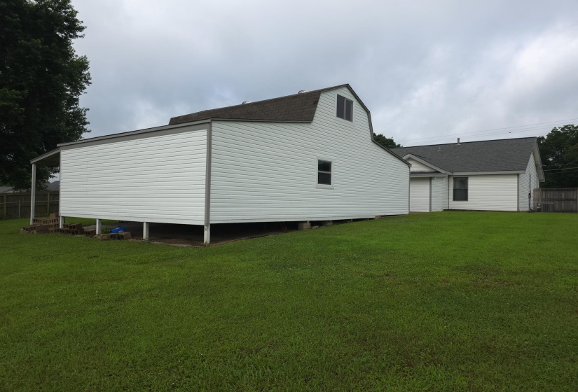 Expansive green lawn featuring a white vinyl-sided outbuilding with a gambrel roof and a covered side porch
