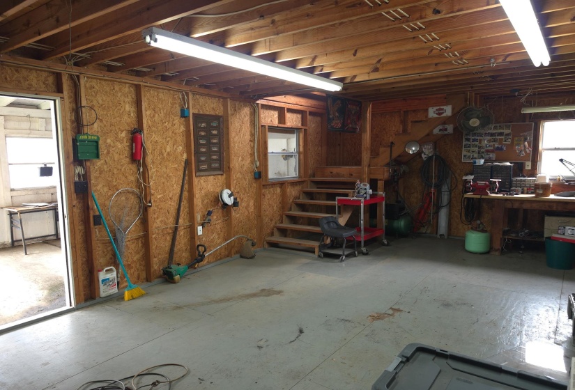 Spacious utility room featuring an exposed beam ceiling, wood-finish wall panels, concrete flooring, and a built-in workbench