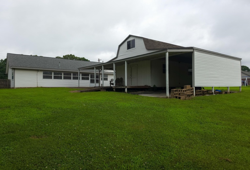 Expansive green lawn with a white vinyl-sided structure featuring an extended covered carport and an upper-level window