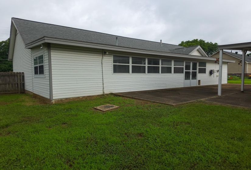 Rear exterior with white vinyl siding, a gray shingle roof, a concrete patio, and a covered concrete carport