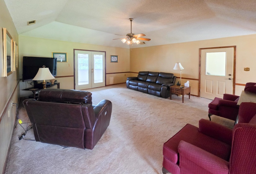 Spacious living area featuring vaulted ceilings, a ceiling fan with integrated lighting, and neutral carpeting