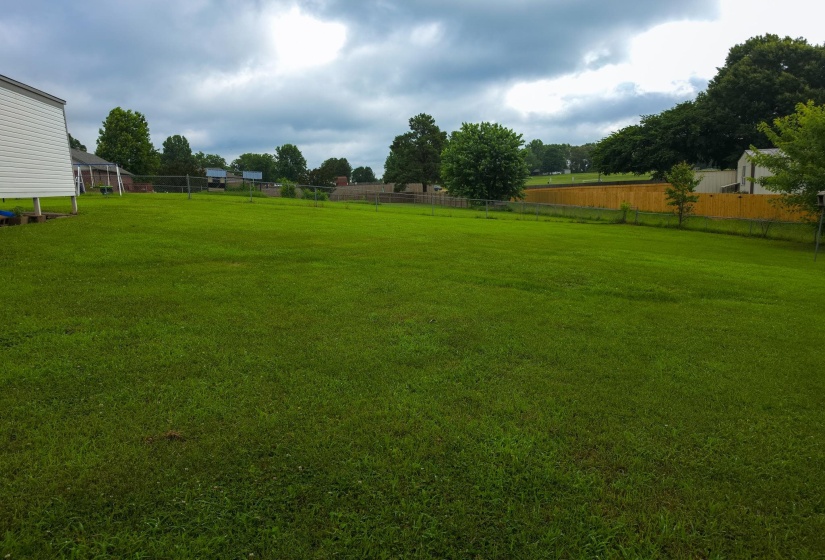 Expansive green lawn with a partial white siding structure and a wood privacy fence