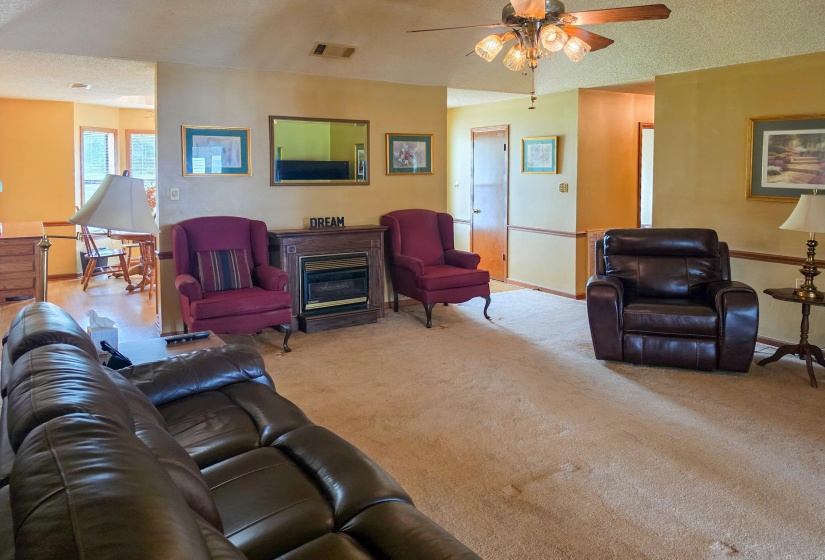 Carpeted living area featuring a decorative electric fireplace with a wood-finish mantel and a ceiling fan with integrated lighting