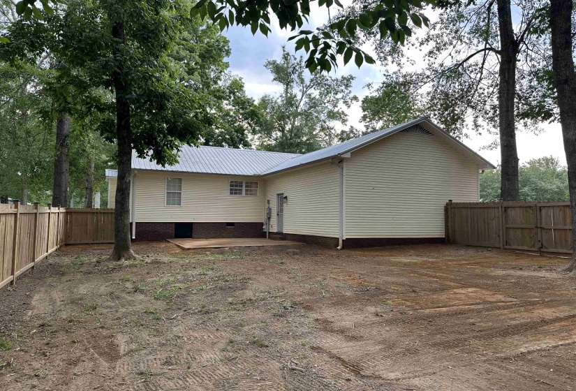 Rear exterior featuring light-colored siding, a metal roof, and a wooden privacy fence enclosing the yard