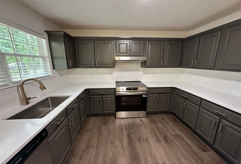 Modern kitchen featuring dark gray cabinetry, light quartz countertops and backsplash, wood-finish flooring, a stainless steel range, and a stainless steel sink with a gooseneck faucet