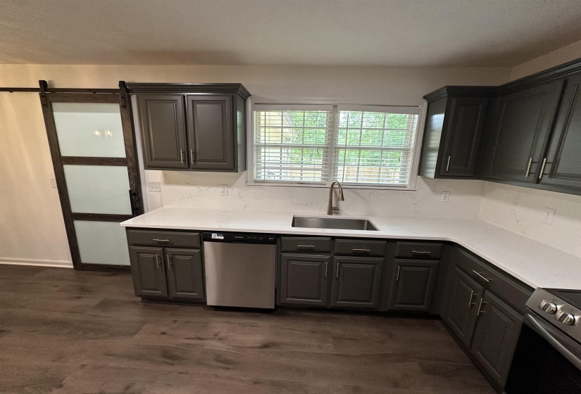 Modern kitchen featuring dark wood-finish cabinetry, stainless steel appliances, and light-toned countertops with a matching backsplash and sliding barn door to laundry room