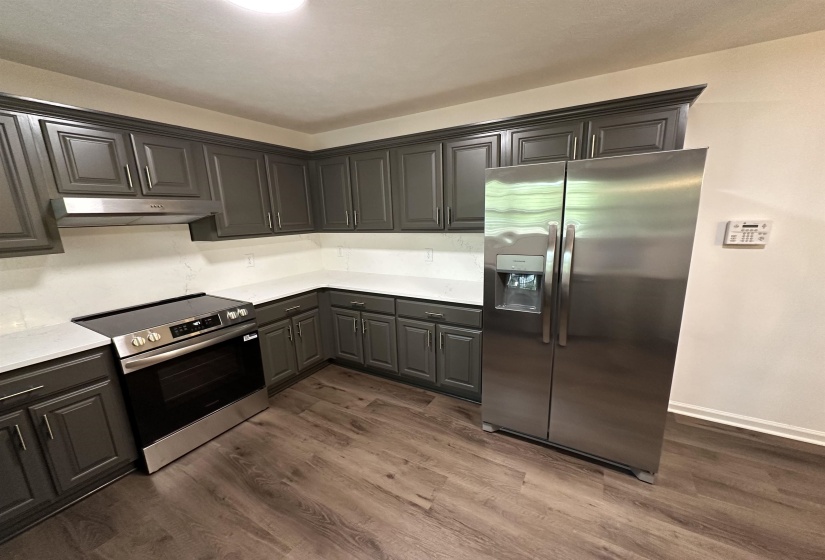 Contemporary kitchen featuring dark gray cabinetry with crown molding, light-toned countertops, and wood-finish flooring