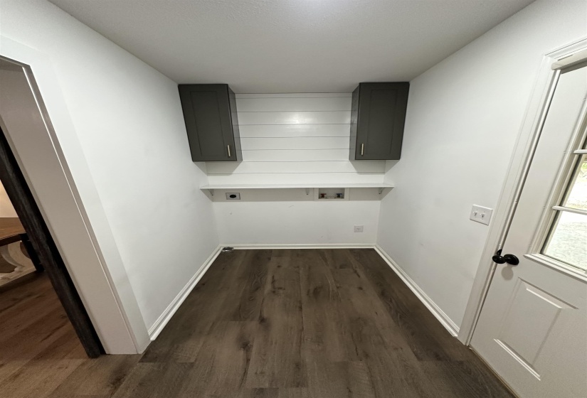 Dedicated utility area featuring wood-finish flooring, white walls, and a white shiplap-style accent wall