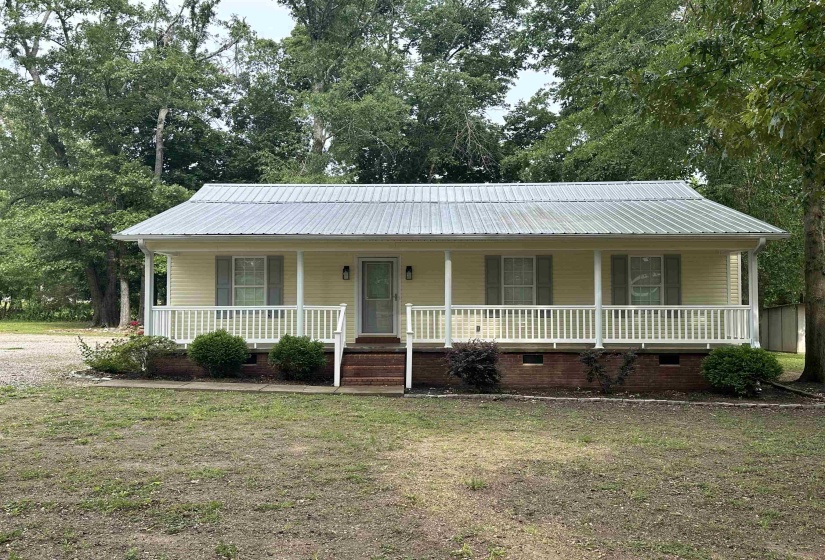 Light colored siding home featuring a covered front porch with white railing, a metal roof, and brick foundation