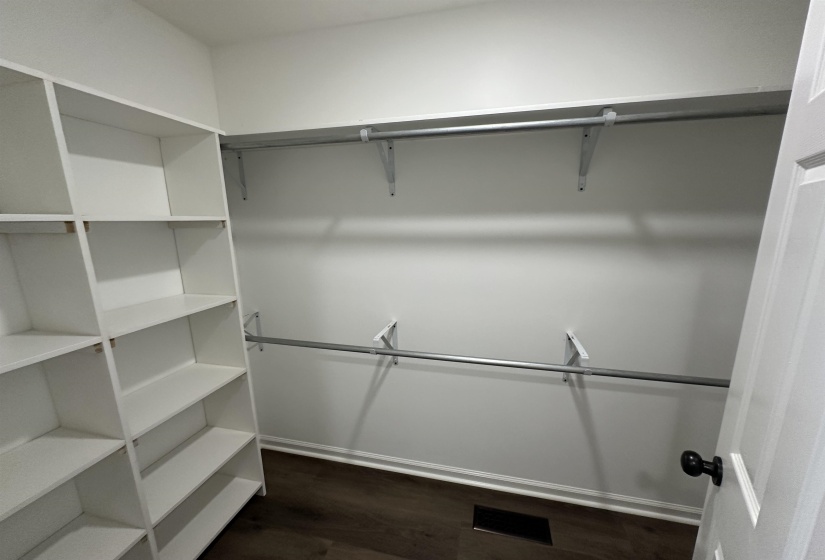 Primary Walk in Closet featuring white built-in shelving, dual chrome hanging rods, wood-finish flooring, white baseboards, and a white interior door with a black knob