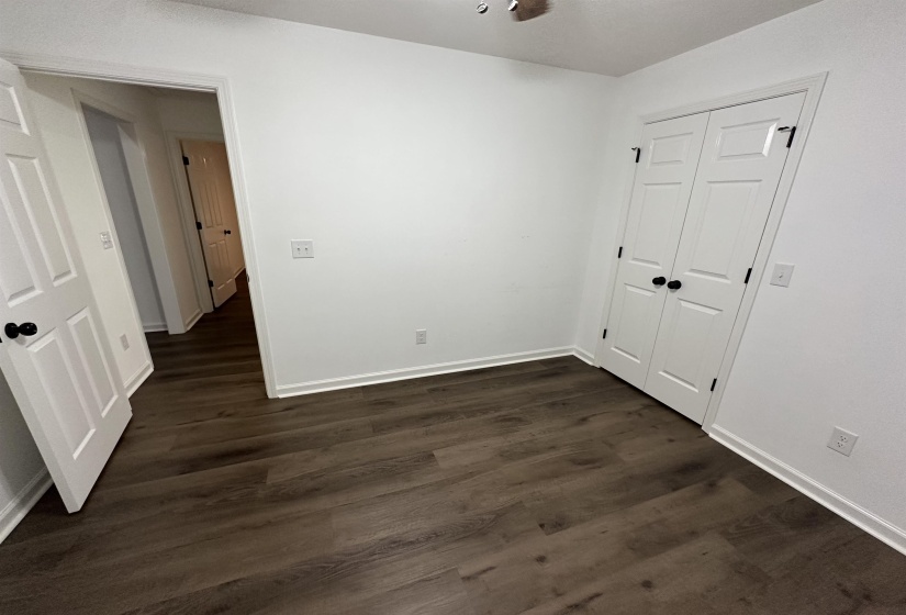 Room featuring wood-finish flooring, white walls, white baseboards, and a white paneled closet with black hardware
