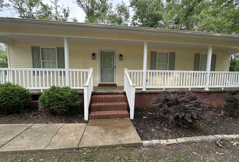 Inviting covered front porch with white railing, brick steps, and yellow siding