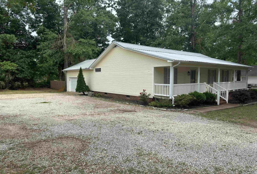 Light colored siding exterior featuring a covered front porch with white railings, a metal roof, and an attached garage