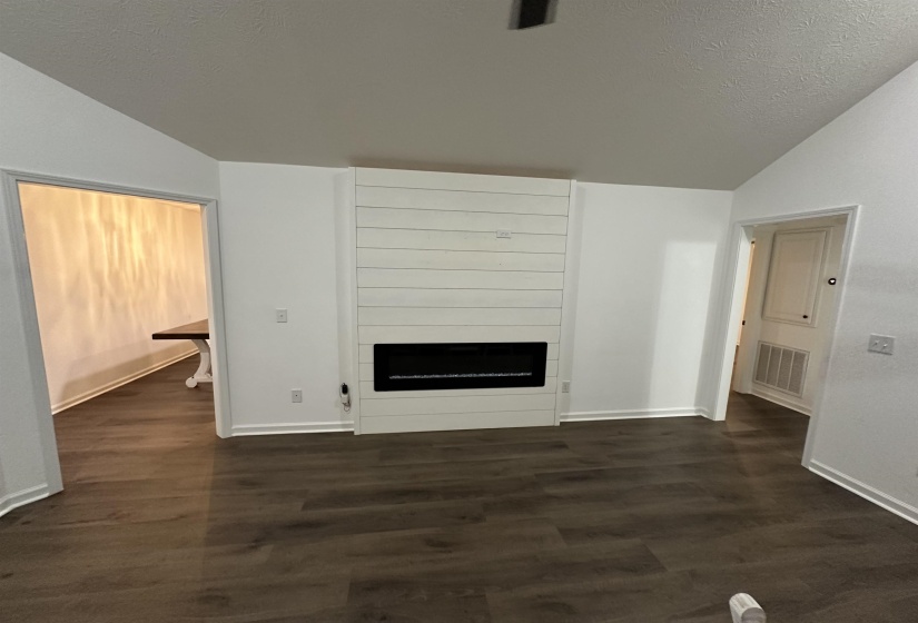 Living area featuring dark wood-finish flooring, a contemporary electric fireplace with a shiplap surround, vaulted ceilings, and white baseboards