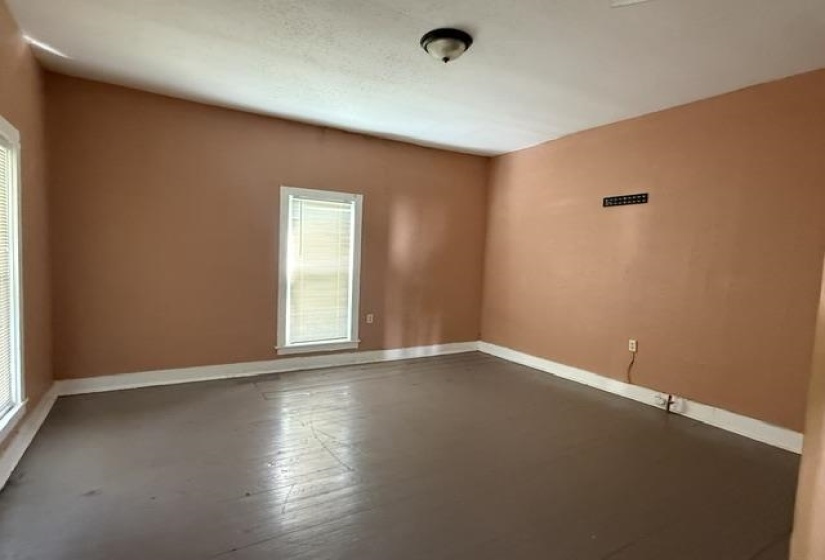 Spacious room featuring two windows with blinds, light peach wall tones, and painted wood-finish flooring