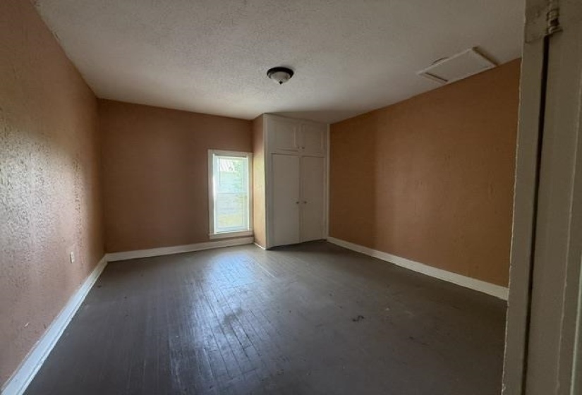Interior room featuring painted wood-finish flooring, a single window with white trim, and a built-in storage cabinet with double doors