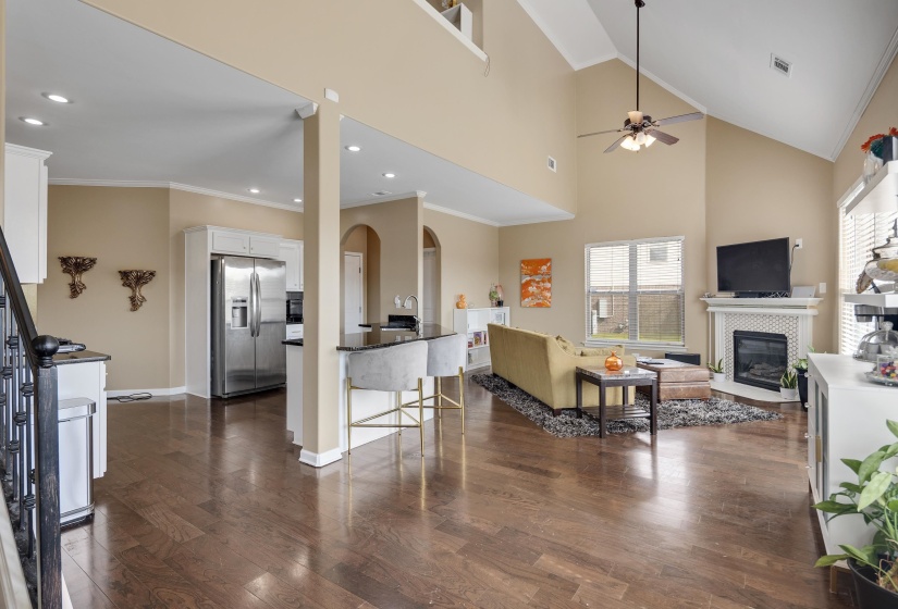 Open-concept living area featuring wood-finish flooring, a vaulted ceiling, and a fireplace with a white mantel