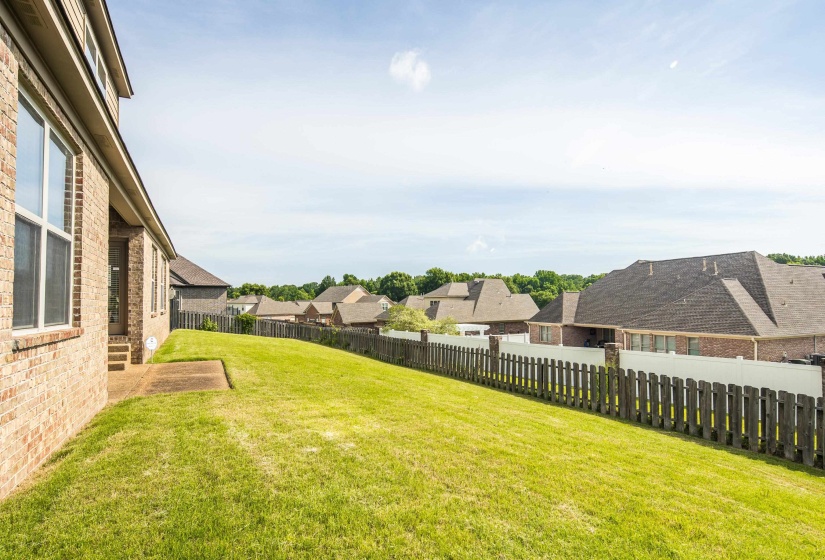 Expansive rear yard featuring green lawn, a privacy fence, and brick exterior with multiple windows