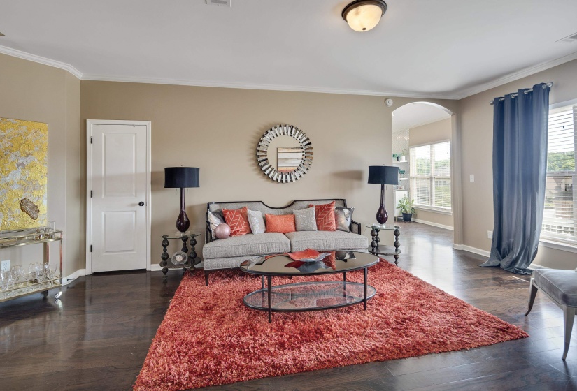 Spacious living area featuring rich wood-finish flooring, crown molding, an arched entryway, and multiple windows with included blinds