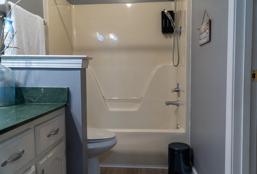 Bathroom featuring a combined shower and tub unit, a toilet, a vanity with a green countertop, and white cabinetry with silver hardware