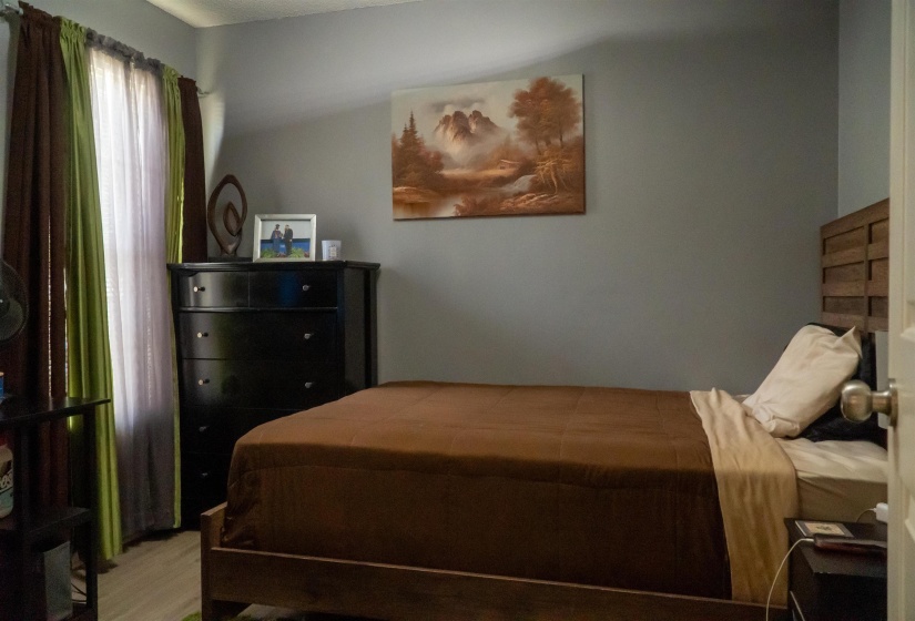 Bedroom featuring light gray walls, wood-finish flooring, and a window with sheer and blackout curtains