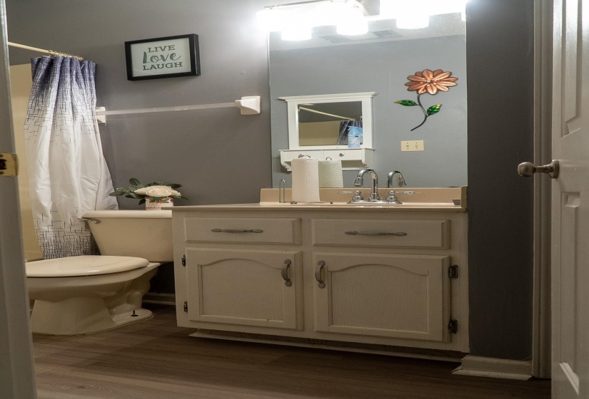 Bathroom featuring a single vanity with a light-colored countertop, white cabinetry with silver hardware, a wall-mounted mirror, and wood-finish flooring
