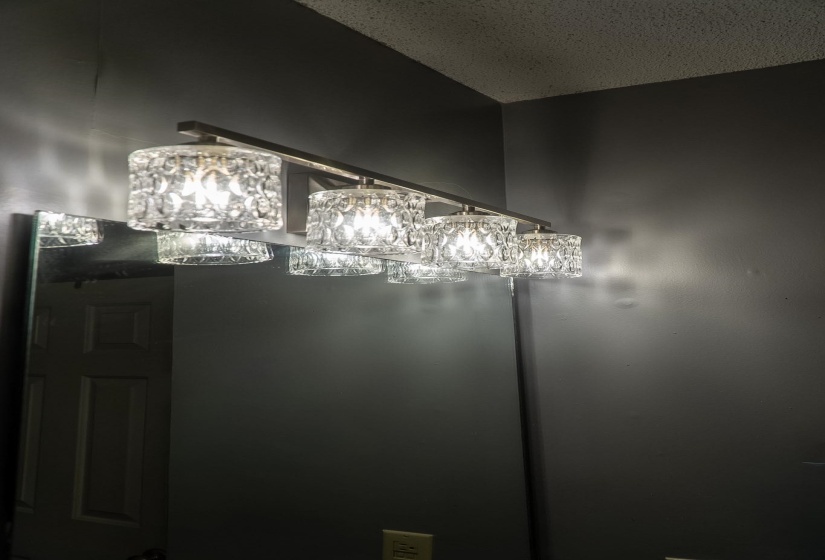 Four-light vanity fixture with clear textured glass shades and a brushed metal base