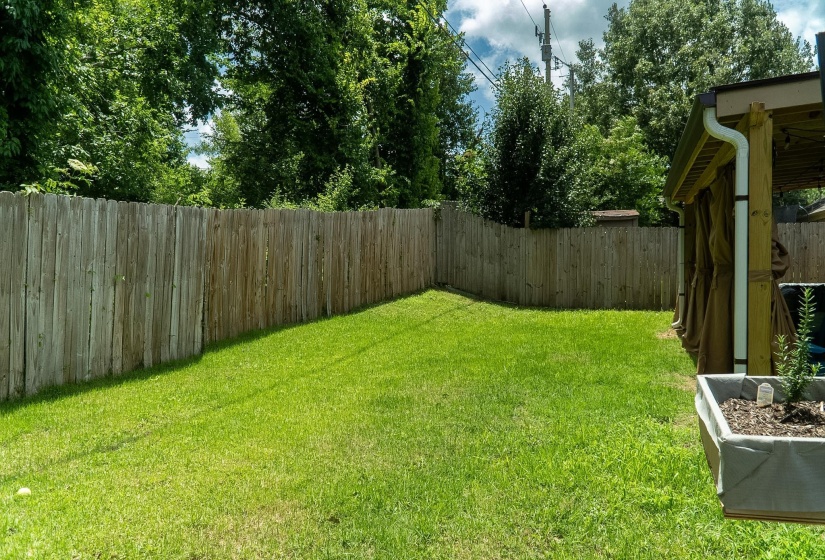 Grassy backyard space bordered by a wooden privacy fence, featuring a raised planter box and a covered patio structure with a gutter system