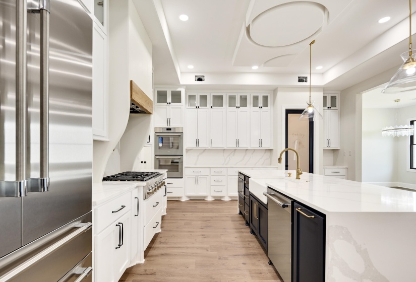 Gourmet kitchen featuring a large central island with a farmhouse sink, stainless steel appliances, extensive white cabinetry, and wood-finish flooring