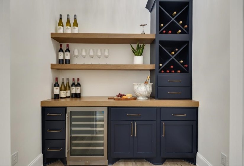 Built-in beverage station featuring a wood-finish countertop, navy cabinetry with gold-tone hardware, and a stainless steel wine refrigerator