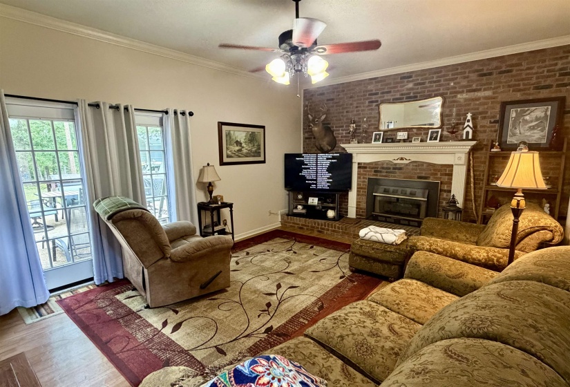 Living area featuring a brick accent wall, white crown molding, and wood-finish flooring