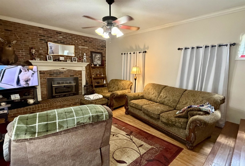 Brick-front fireplace with a white mantel and hearth, featuring wood-finish flooring and crown molding