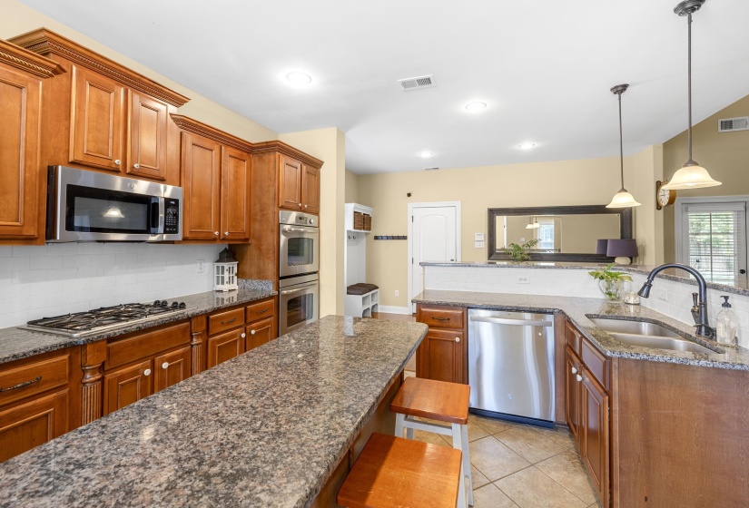 Kitchen featuring wood cabinetry, granite countertops, stainless steel appliances, tiled flooring, and pendant lighting