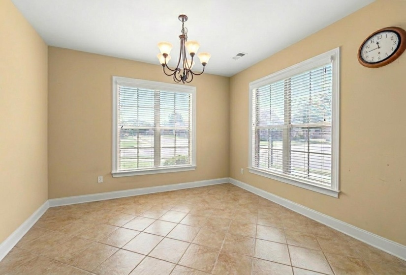 Spacious room featuring tile flooring, neutral wall tones, two large windows with blinds, a multi-light chandelier, and white baseboards