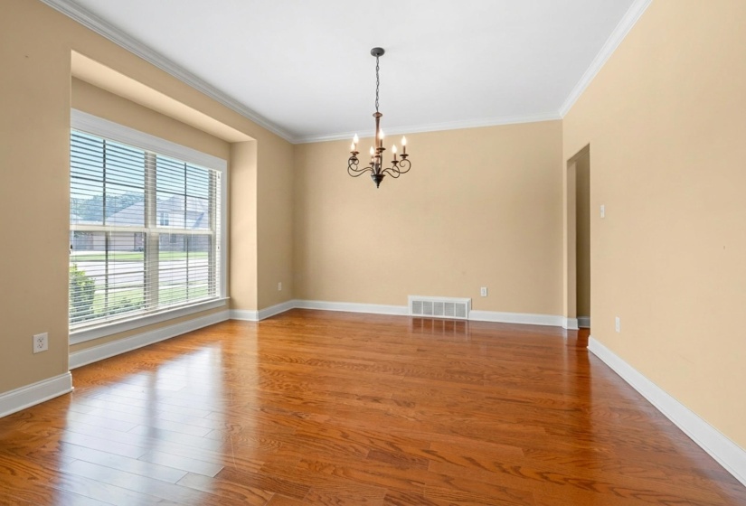 Spacious room featuring rich wood-finish flooring, a large bay window, and a classic chandelier
