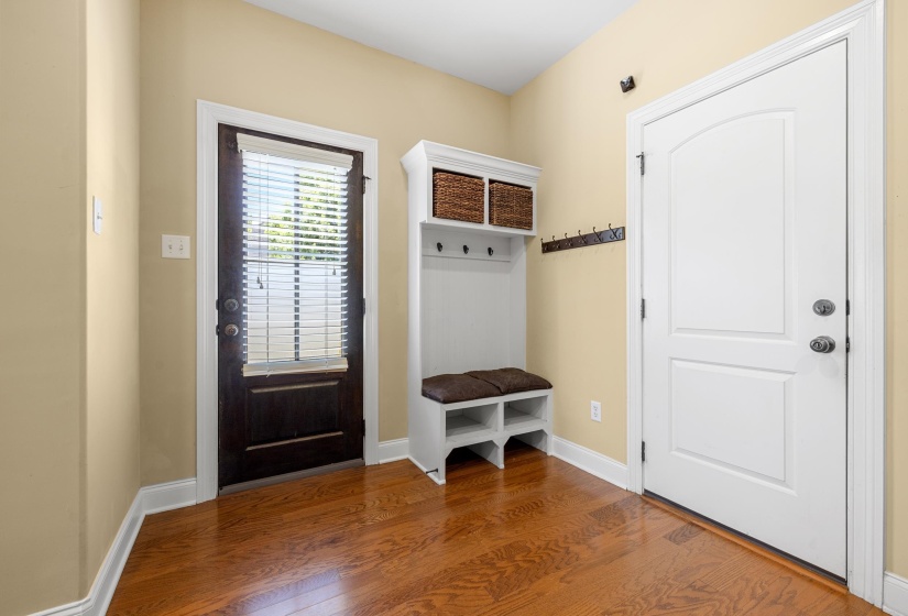 Entryway featuring wood-finish flooring, a built-in hall tree with storage, a dark-paneled exterior door with blinds, and a white paneled interior door