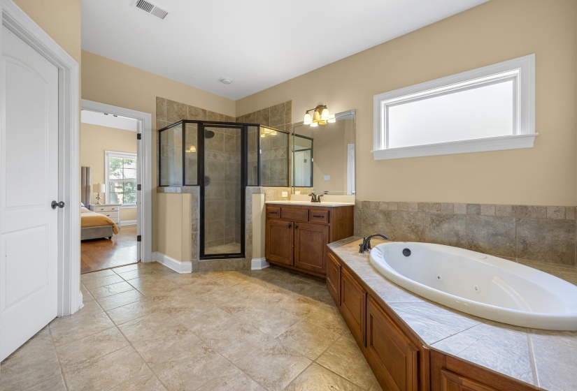 Bathroom featuring a built-in soaking tub with tiled surround, a walk-in shower with glass enclosure, a single vanity with wood cabinetry, and tiled flooring