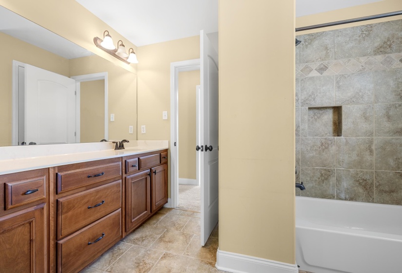 Bathroom featuring a double vanity with wood cabinetry, a large mirror, and a tiled shower-tub combination with a recessed niche