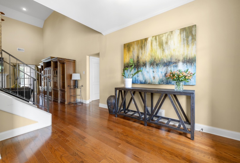 Foyer featuring high vaulted ceilings, wood-finish flooring, a white trim baseboard, and a staircase with an iron railing