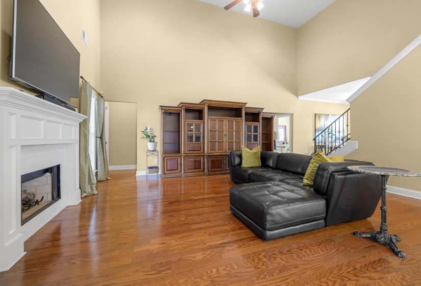 Living area featuring vaulted ceilings, wood-finish flooring, a white mantel fireplace, and a staircase with a black wrought iron railing