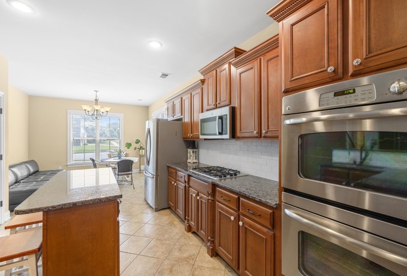 Kitchen featuring wood cabinetry, granite countertops, tile flooring, and stainless steel appliances including a built-in double oven, gas cooktop, and microwave