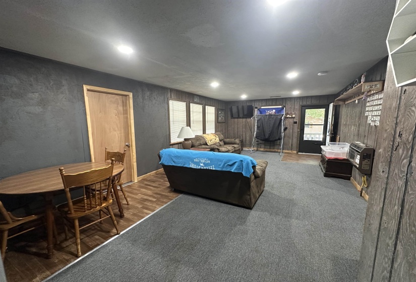 Spacious room featuring recessed ceiling lights, dark-toned textured wall treatment, and mixed flooring of wood-finish planks and grey carpeting