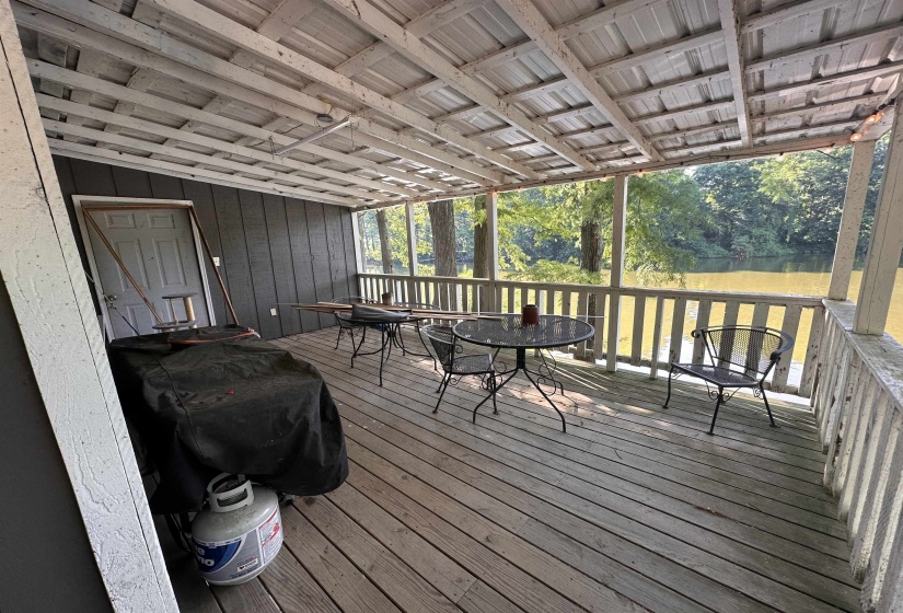 Covered deck with wood-finish flooring and slatted railing overlooking a body of water