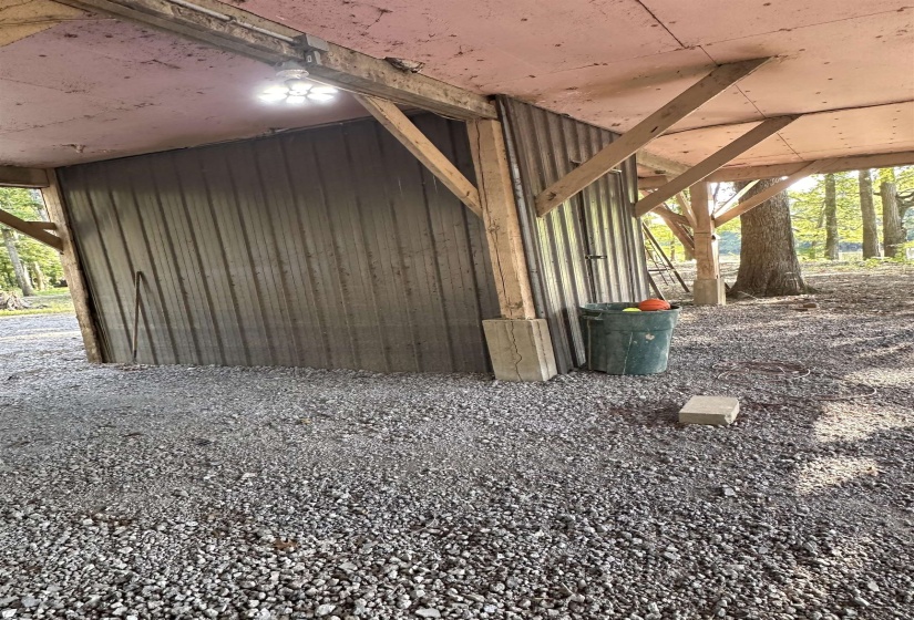 Sheltered outdoor area featuring a gravel surface, exposed wood structural beams, and a corrugated metal wall