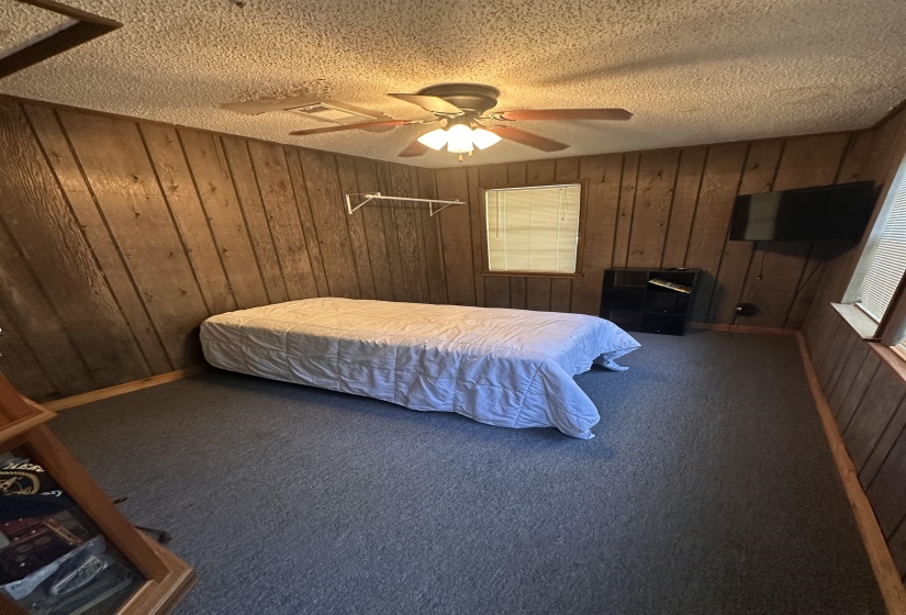 Room featuring wood paneling, carpeted flooring, a ceiling fan with integrated lighting, and a single window with blinds