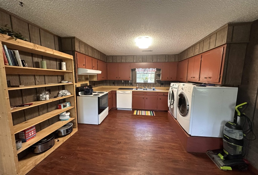Kitchen and utility area featuring wood-finish flooring, wood paneling, and an exposed shelving unit