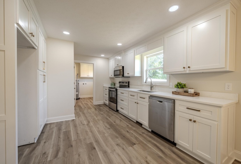 Bright kitchen featuring extensive white cabinetry, recessed lighting, wood-finish flooring, stainless steel appliances, and a window above the sink