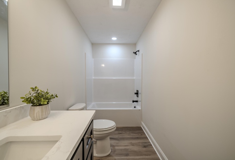 Bathroom featuring a white tub-shower combination with black fixtures, dark wood-finish vanity with a white countertop, and wood-finish flooring